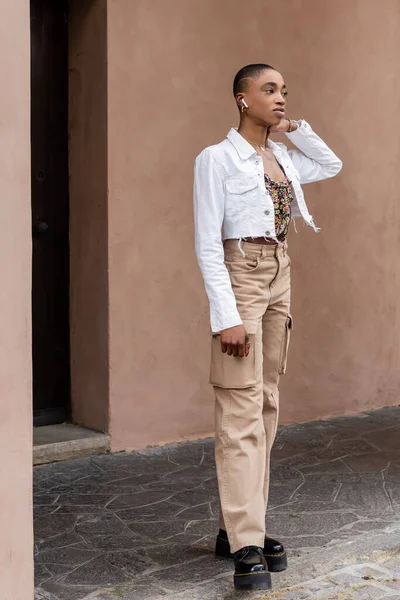 Mujer afroamericana de moda usando auriculares inalámbricos en la calle urbana de Treviso - foto de stock