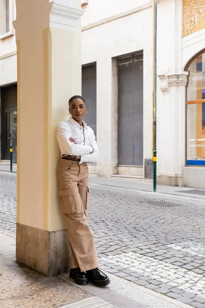 Trendy african american woman crossing arms and looking at camera on urban street in Treviso — Stock Photo