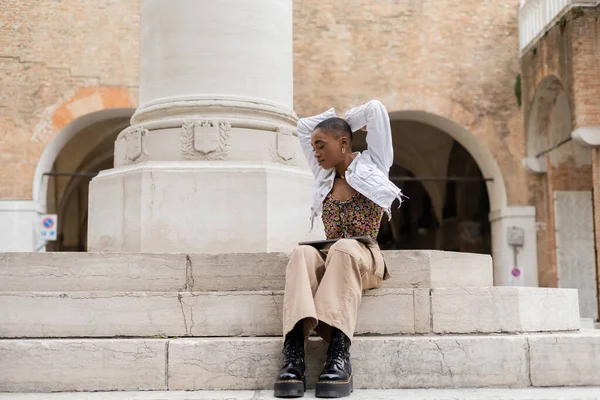 Blogger afroamericano di tendenza con laptop seduto sulle scale in strada urbana in Italia — Foto stock