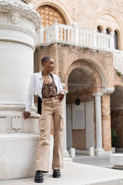 Joven mujer afroamericana de pelo corto de pie cerca del viejo edificio en la calle urbana de Treviso - foto de stock