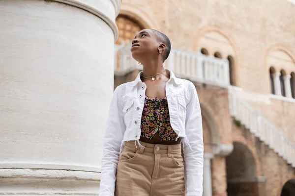 Stylish african american woman looking away near building on urban street in Treviso — Stock Photo