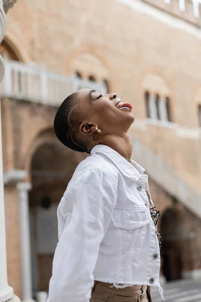 Side view of stylish african american woman sticking out tongue on urban street in Treviso — Stock Photo