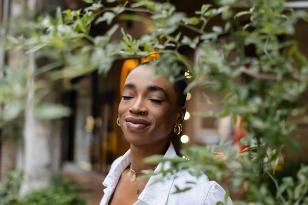 Fashionable african american woman standing near tree on urban street — Stock Photo