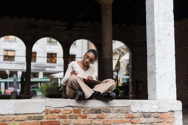 Stilvolle Afroamerikanerin schreibt auf Notizbuch auf urbaner Straße in Treviso — Stockfoto