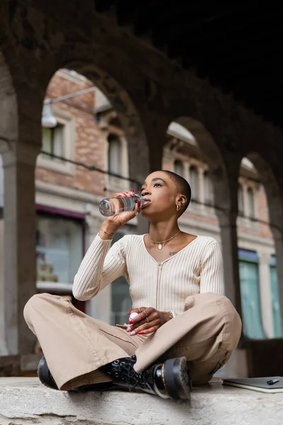 Стильна афро-американська жінка п'є воду біля записника на міській вулиці в Тревізо. — стокове фото