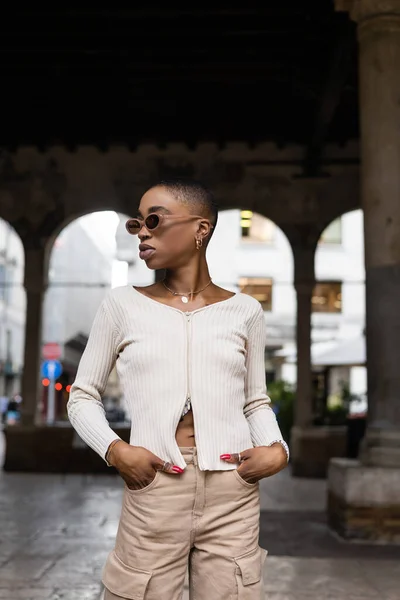 Donna afroamericana alla moda in occhiali da sole che si tiene per mano in tasche di pantaloni all'aperto a Treviso — Foto stock