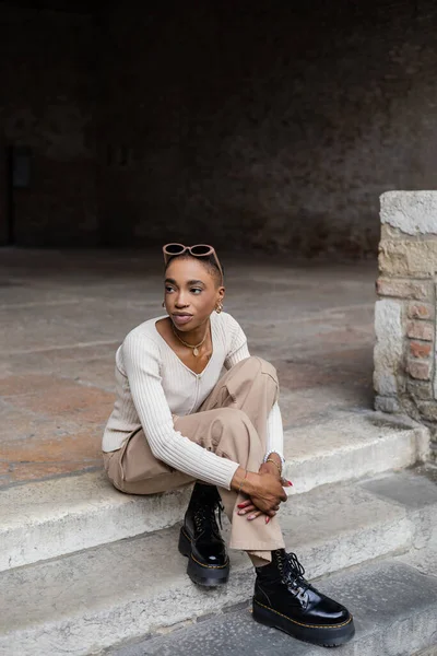 Trendy african american woman with sunglasses sitting on stairs on urban street in Treviso — Stock Photo