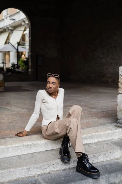 Stylish african american woman with sunglasses sitting on stairs on urban street in Treviso — Stock Photo