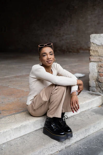 Femme afro-américaine à la mode en lunettes de soleil regardant la caméra sur les escaliers à l'extérieur — Photo de stock