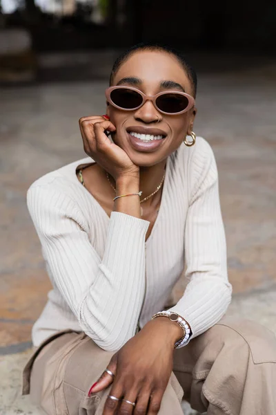 Modische Afroamerikanerin mit Sonnenbrille lächelt auf verschwommener Straße — Stockfoto