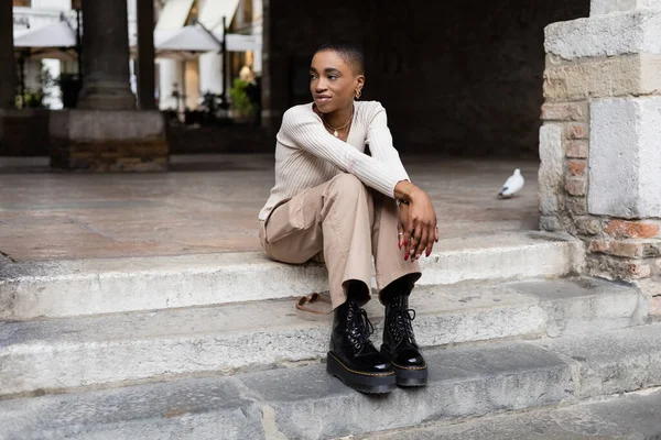 Fashionable african american woman sitting on stairs on city street in Italy — Stock Photo