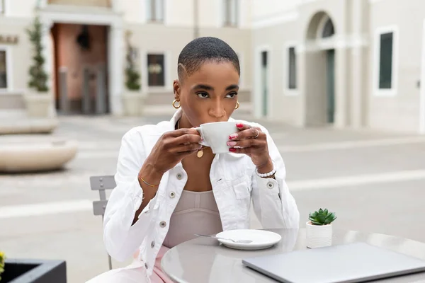 Blogueur afro-américain élégant boire du café près d'un ordinateur portable dans un café en plein air en Italie — Photo de stock