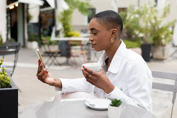 Стильная африканская американка с чашкой капучино и смартфоном на городской улице в Тревизо — стоковое фото