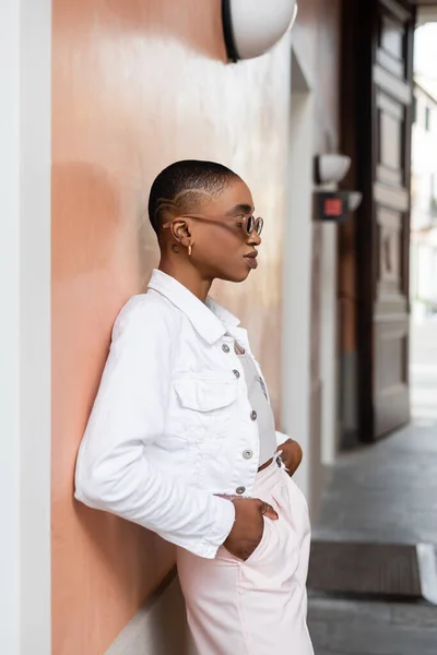 Бічний вид на афроамериканку в сонцезахисних окулярах, що сидять біля будинку на вулиці в Тревізо. — стокове фото