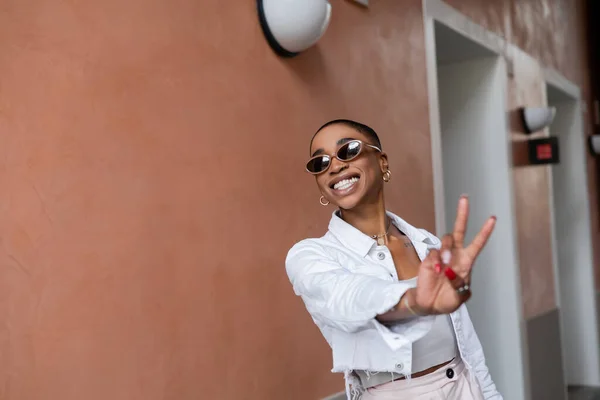 Веселая и стильная африканская американка показывает знак мира на городской улице — стоковое фото