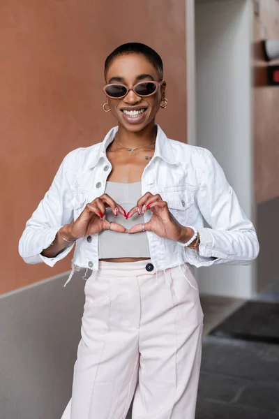 Lächelnde Afroamerikanerin mit Sonnenbrille zeigt Liebeszeichen auf urbaner Straße — Stockfoto