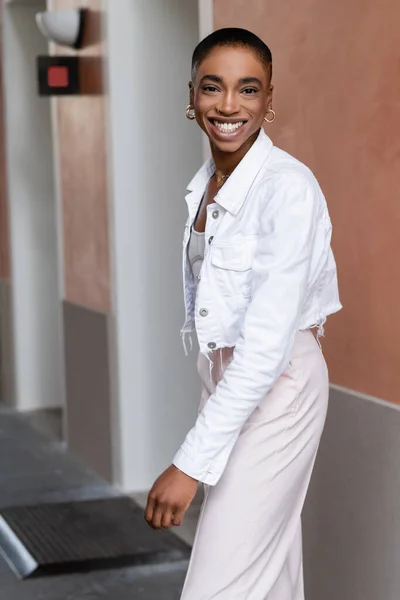 Счастливая африканская американка в стильной белой куртке, смотрящая в камеру на городской улице в Тревизо — стоковое фото