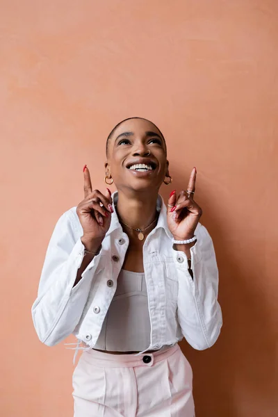 Счастливая африканская американка в стильной одежде, указывающая пальцами на стену — стоковое фото