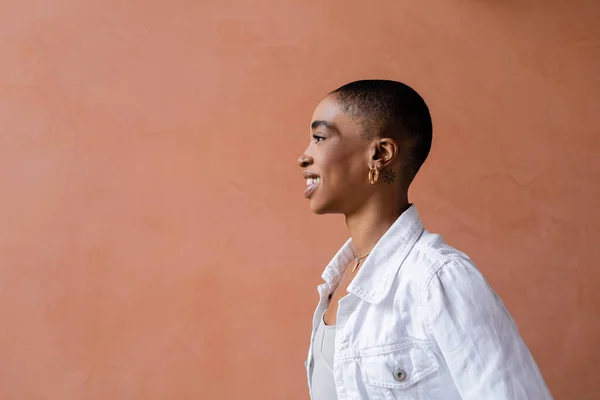 Vue latérale de souriante femme afro-américaine aux cheveux courts debout près du mur à l'extérieur — Photo de stock