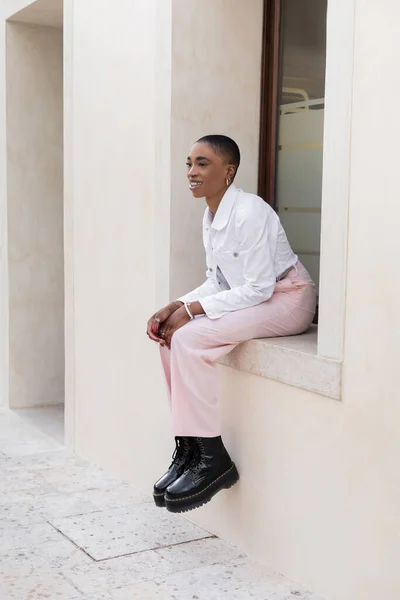 Short haired african american woman smiling while sitting on windowsill of building outdoors in Treviso — Stock Photo