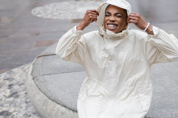 Счастливая и стильная африканская американка в плаще закрывает глаза на городскую улицу — стоковое фото
