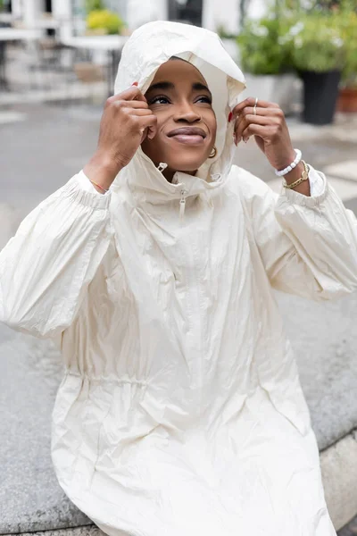 Fashionable african american woman in raincoat looking away on urban street — Stock Photo