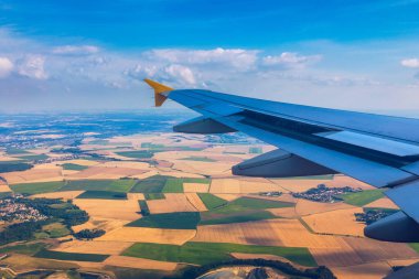 Yolcu penceresinden mavi gökyüzünün altında yüksek irtifada bulutların üzerinde uçan bir uçağın kanadının görüntüsü. Avrupa üzerinde uçarken. Bulutların üzerinde mavi gökyüzünde uçan jet uçağı kanadı görüntüsü.
