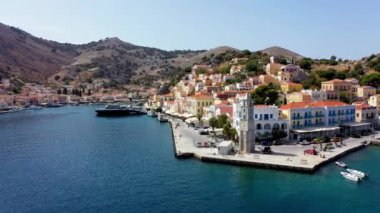 Symi (Simi) ada limanı, klasik gemi yatları, ada tepelerindeki evler, Ege Körfezi manzarası. Yunanistan adaları Rodos adasından tatil turları düzenliyor. Symi, Yunanistan, Dodecanese.