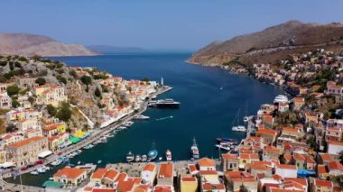 Symi (Simi) ada limanı, klasik gemi yatları, ada tepelerindeki evler, Ege Körfezi manzarası. Yunanistan adaları Rodos adasından tatil turları düzenliyor. Symi, Yunanistan, Dodecanese.