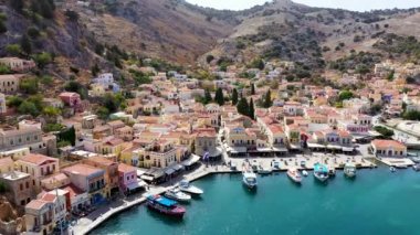 Symi (Simi) ada limanı, klasik gemi yatları, ada tepelerindeki evler, Ege Körfezi manzarası. Yunanistan adaları Rodos adasından tatil turları düzenliyor. Symi, Yunanistan, Dodecanese.