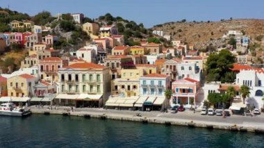 Symi (Simi) ada limanı, klasik gemi yatları, ada tepelerindeki evler, Ege Körfezi manzarası. Yunanistan adaları Rodos adasından tatil turları düzenliyor. Symi, Yunanistan, Dodecanese.