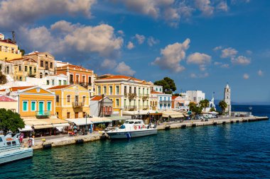Symi (Simi) ada limanı, klasik gemi yatları, ada tepelerindeki evler, Ege Körfezi manzarası. Yunanistan adaları Rodos adasından tatil turları düzenliyor. Symi, Yunanistan, Dodecanese.