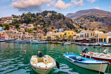 Symi (Simi) ada limanı, klasik gemi yatları, ada tepelerindeki evler, Ege Körfezi manzarası. Yunanistan adaları Rodos adasından tatil turları düzenliyor. Symi, Yunanistan, Dodecanese.