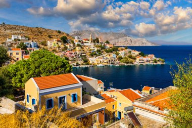 Symi (Simi) ada limanı, klasik gemi yatları, ada tepelerindeki evler, Ege Körfezi manzarası. Yunanistan adaları Rodos adasından tatil turları düzenliyor. Symi, Yunanistan, Dodecanese.