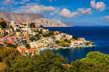Symi (Simi) ada limanı, klasik gemi yatları, ada tepelerindeki evler, Ege Körfezi manzarası. Yunanistan adaları Rodos adasından tatil turları düzenliyor. Symi, Yunanistan, Dodecanese.