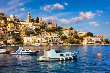 Symi (Simi) ada limanı, klasik gemi yatları, ada tepelerindeki evler, Ege Körfezi manzarası. Yunanistan adaları Rodos adasından tatil turları düzenliyor. Symi, Yunanistan, Dodecanese.