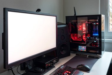 Powerful personal computer gamer rig with white screen. Professsional gaming empty room studio with neon lights and RGB powerful computer, keyboard and mouse. White screen on pc display.