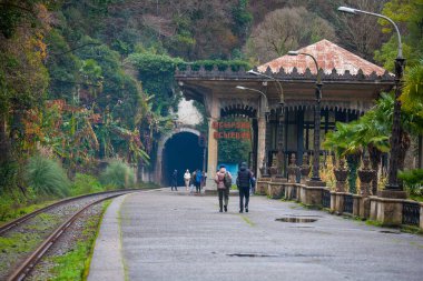 Turistler terk edilmiş tren istasyonu boyunca yürüyorlar Psyrdzkha, Abhazya