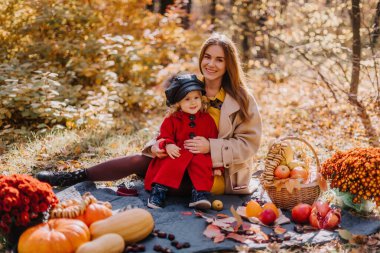 Anne ve kızı, sonbahar ormanlarında sonbahar meyveleriyle birlikte bir paspasın üzerinde oturuyorlar.