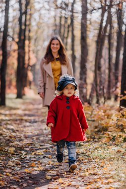 Sonbaharda ormanda kırmızı ceketli bir anne ve kız yürür.