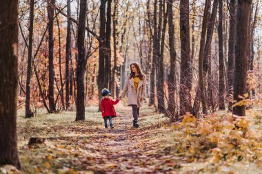 Mom and daughter in a red coat walk in forest in autumn