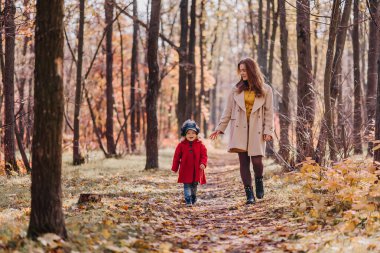 Mom and daughter in a red coat walk in forest in autumn