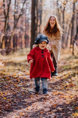 Anne ve kızı sonbahar ormanlarında oynuyorlar.