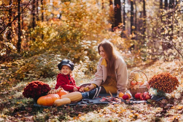 Mom and daughter sit on a mat with autumn fruits in the autumn forest
