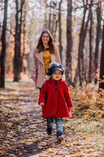 Mom and daughter in a red coat walk in forest in autumn