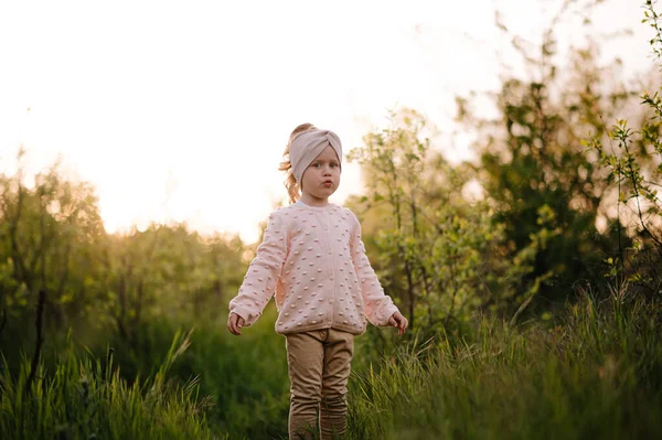 Little girl have fun in a hight green grass in the sunset