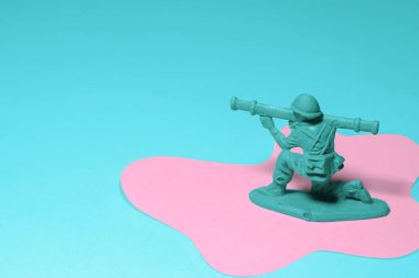 Elinde silah olan minyatür oyuncak asker, pembe mavi arka plan.