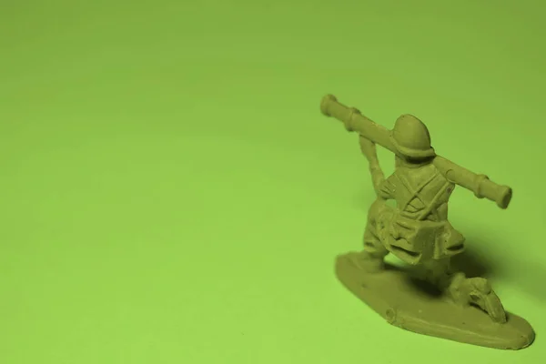 Miniature toy soldier with weapon in hand, green background