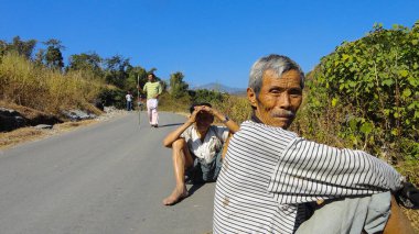 İki yaşlı adam sohbet oturumunda Batı Bengal 'deki dik bir tepe yolunda oturuyorlar. Turistler arkada..