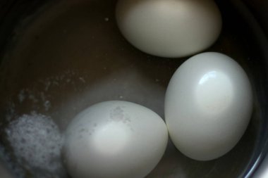 Üç haşlanmış yumurta sıcak su dolu paslanmaz çelik kap.